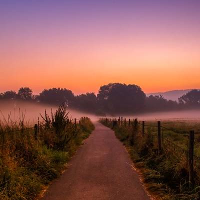 Misty rural path at sunrise with colorful sky.