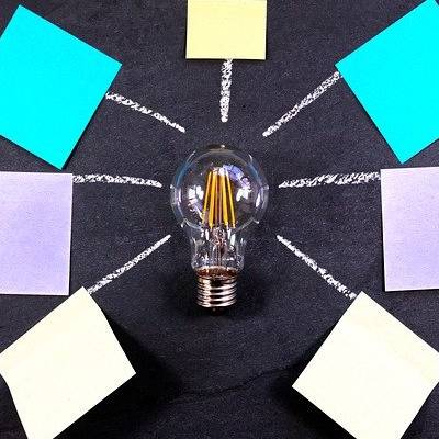 Ampoule entourée de post-its colorés sur tableau noir.